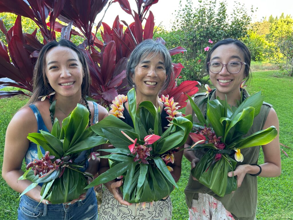 Three people smiling while holding Ti-leaf bundles